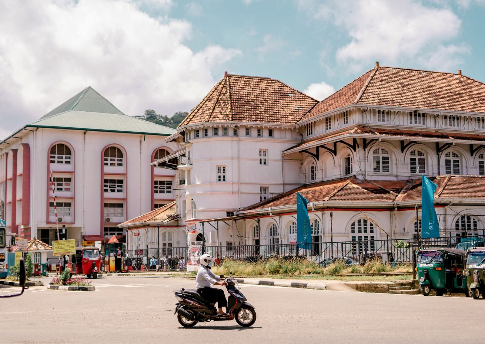 A vibrant street scene in Kandy, Sri Lanka featuring a historic building and a scooter rider.